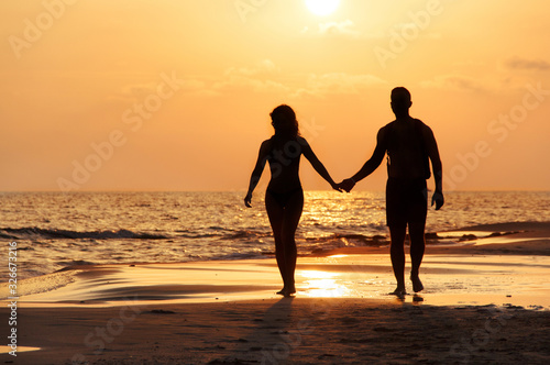 Silhouette of a couple walking at the beach in front of the sunset
