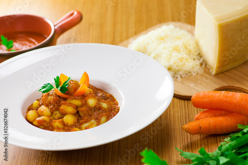 plato de gnocchi italiano al ragú con tomate y zanahoria sobre tabla de madera rodeado por los ingredientes frescos