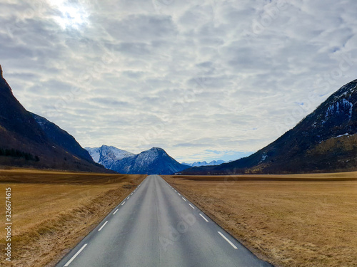 Straight asphalt road between field and mountains leading to nowhere