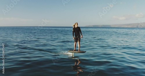 Aerial view of a young man riding on an electric hydrofoil surfboard on glassy blue ocean water, the future of green electric personal watercraft is hydrofoiling photo