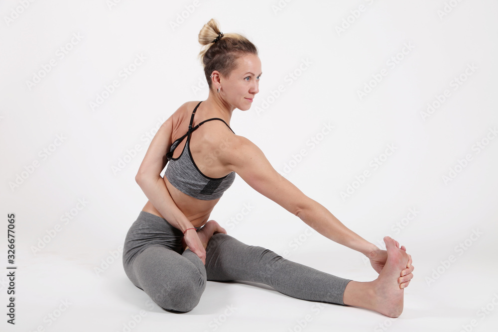 Obraz premium Young woman practicing yoga,standing in exercise leaning forward to straight legs, holding hands,toes, marichiasana II pose, balance workout,sportswear, pants,short,studio,white grey background