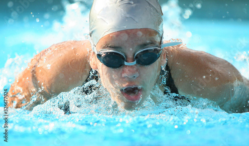 nadadora competindo de touca e óculos na piscina, nado borboleta na direção da câmera, ombros a mostra photo