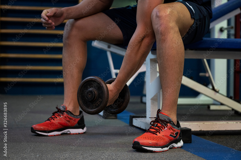 young athlete sitting on a bench and lifting weights in a gym