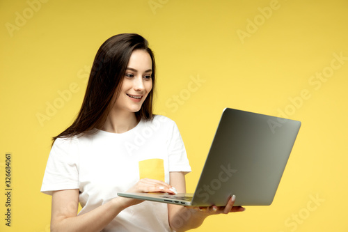 woman with laptop on yellow background, copy space.