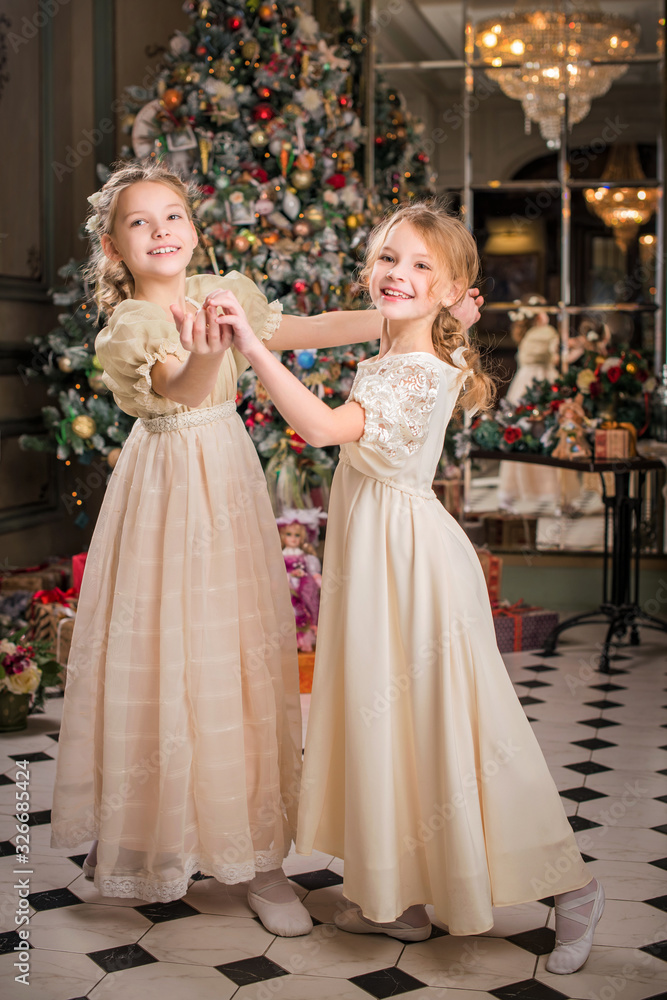 Two smartly dressed girls are playing a Christmas tale at home.