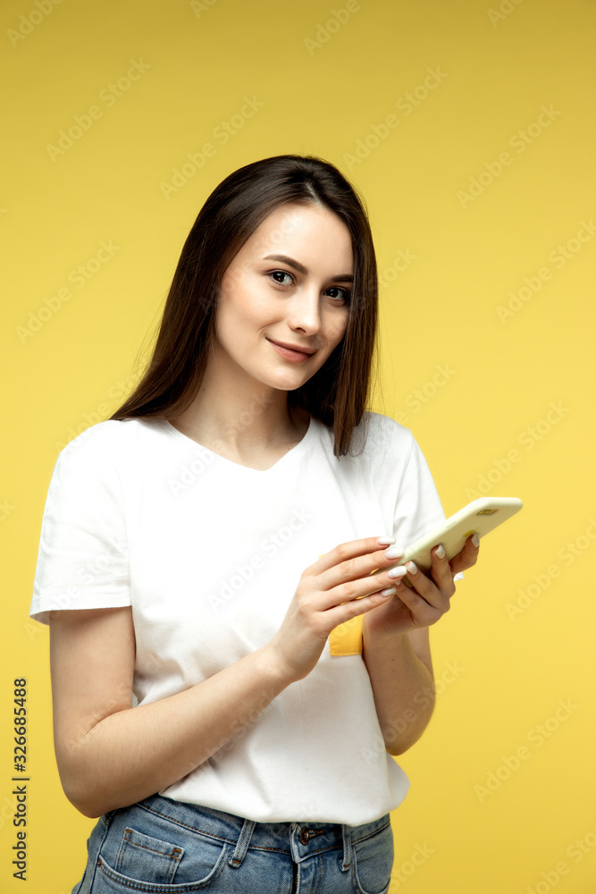 Surprised young girl in fur sweater posing isolated on yellow orange background, studio portrait. People lifestyle concept. Mock up copy space. Using mobile phone, typing sms message Surprised young girl in fur sweater posing isolated on yellow orange background, studio portrait. People lifestyle concept. Mock up copy space. Using mobile phone, typing sms message