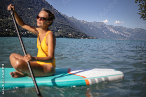 Pretty, young woman paddling on a paddle board on a lake, enjoying a lovely summer day