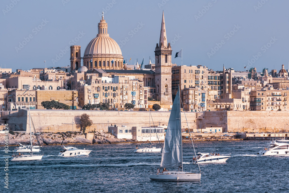 White yacht and boats in harbor of Valletta, Our Lady of Mount Carmel church and St. Paul's Anglican Pro-Cathedral on the background, Valletta, Malta