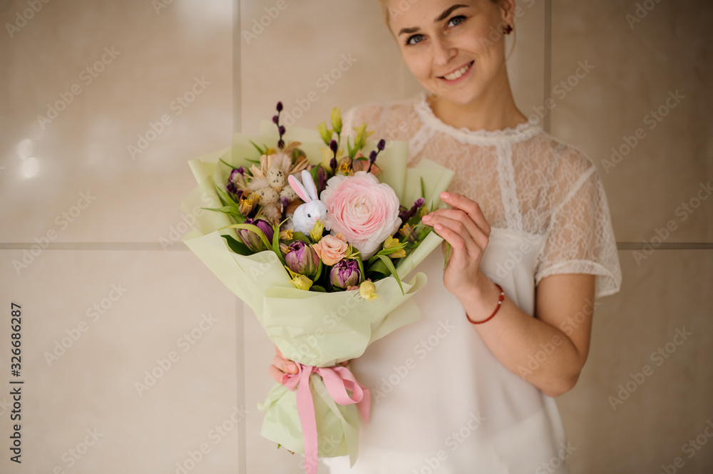 Girl holding a spring bouquet of different flowers decorated with dark willow branches, little toy rabbit wrapped in green paper Girl holding a spring bouquet of different flowers decorated with dark willow branches, little toy rabbit wrapped in green paper