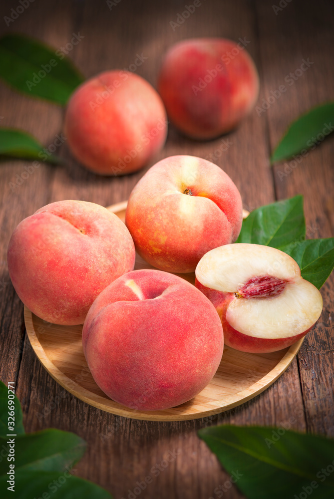 Ripe peaches with leaves on the old wooden table.Fresh Japan Peaches wooden plate in wooden Background Ripe peaches with leaves on the old wooden table.Fresh Japan Peaches wooden plate in wooden Background