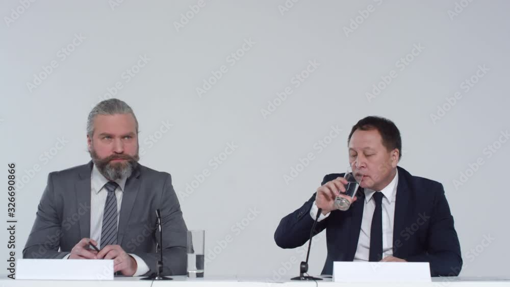 Lockdown of two elderly multiethnic spokesmen sitting at table in conference room and having talk with journalists Lockdown of two elderly multiethnic spokesmen sitting at table in conference room and having talk with journalists