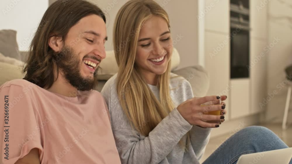 A happy positive couple man and woman in casual wear are having a video call on the silver laptop computer in the living room at home A happy positive couple man and woman in casual wear are having a video call on the silver laptop computer in the living room at home