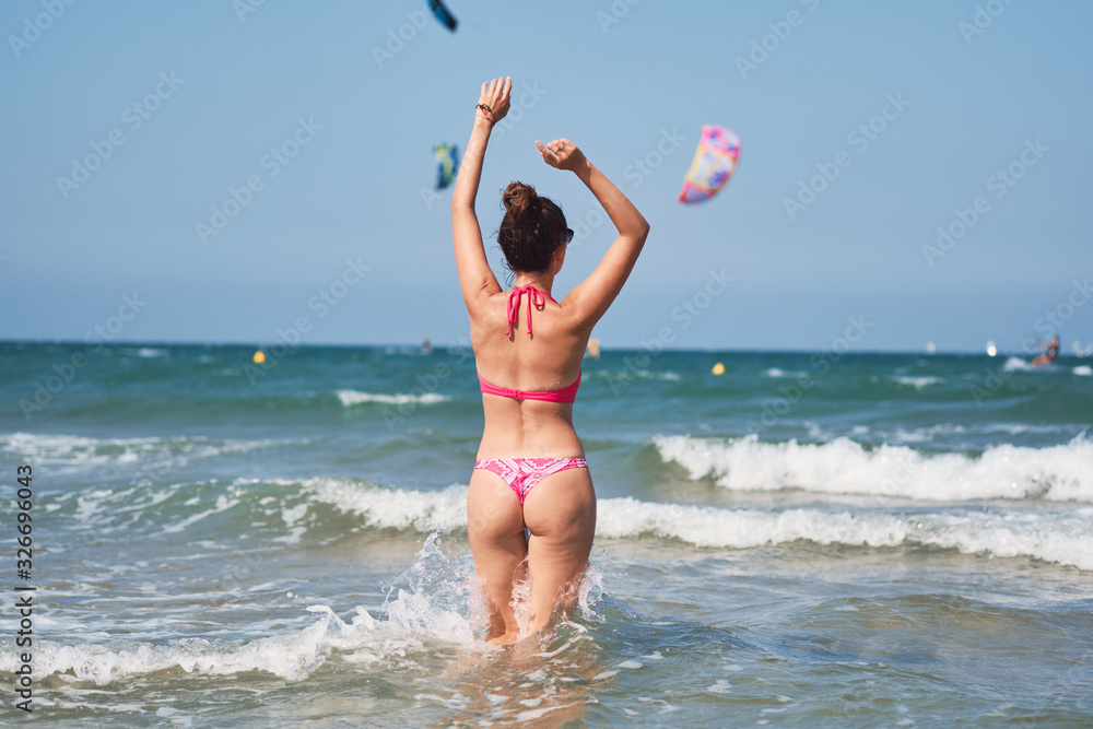 Back view of young woman in pink bikini enjoying the wavy sea during her vacation. Back view of young woman in pink bikini enjoying the wavy sea during her vacation.