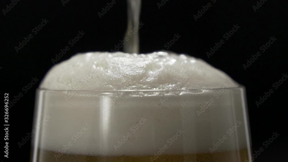 Beer is poured into a glass with white foam. Beer settling in a glass