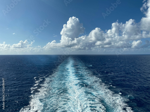 Seascape. Beautiful view of the horizon of the sea and sky with white clouds. White path of waves from the movement of the ship. Cropped shot, horizontal, free space. The concept of rest and travel.