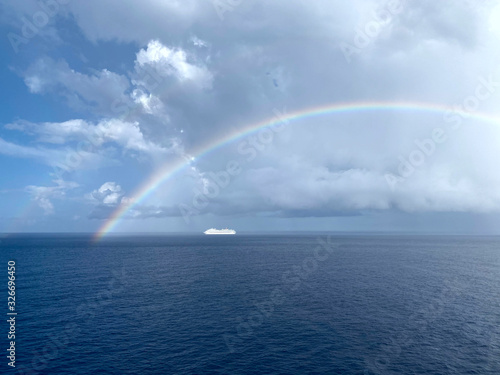 Blurred marine landscape. Beautiful view of the sea horizon with a white ship and a rainbow. Background of blue sky  ocean and rainbow. Cadded shot  horizontal  free space. Concept of rest and travel.