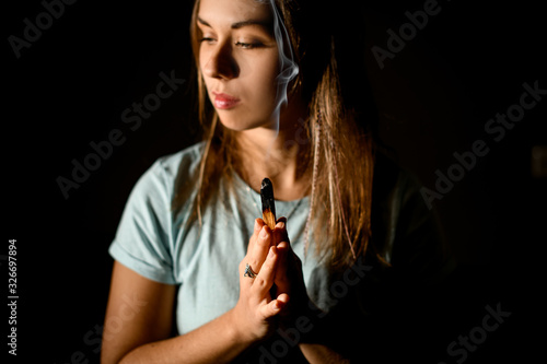 Woman practicing yoga in a studio room hold hands in namaste holding a palo santo