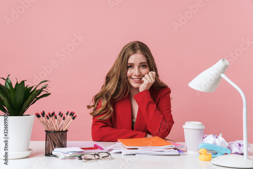 Woman sit at the table over pink wall background.