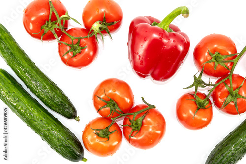 Top view of fresh vegetables: large green cucumbers, one red bell pepper, red tomatoes on a green branch