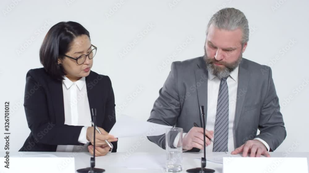 Tracking right of two diverse women and grey-haired Caucasian man wearing elegant clothes sitting at long table during official conference and discussing document Tracking right of two diverse women and grey-haired Caucasian man wearing elegant clothes sitting at long table during official conference and discussing document