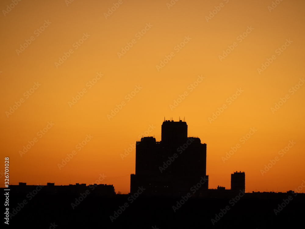 Skyscraper tower silhouette over dark forest on sunset and clear orange tone sky as background. Sunny weather (Moscow city, Russia)