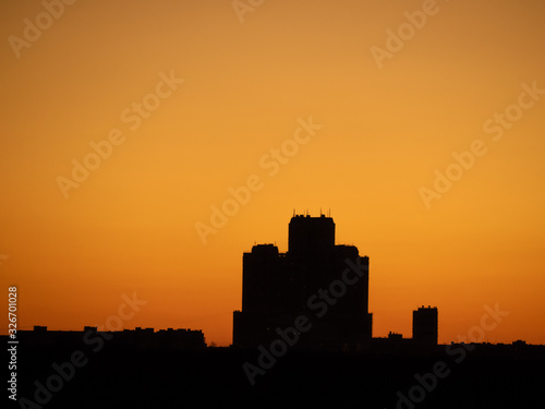 Skyscraper tower silhouette over dark forest on sunset and clear orange tone sky as background. Sunny weather (Moscow city, Russia)