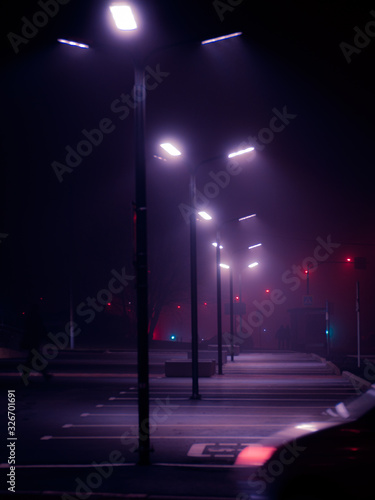 Photography Modern street lights in the fog on empty parking in the night and fragment of the blurred car silhouette on foreground