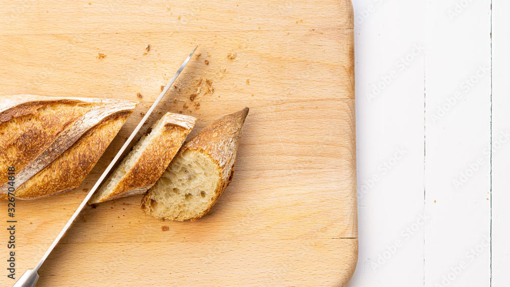 Cut French baguettes, bread with a knife on a wooden cutting board. Close up. On a left side. Copy space. Top view. Concept: healthy live, bakery, french tradition food. Cut French baguettes, bread with a knife on a wooden cutting board. Close up. On a left side. Copy space. Top view. Concept: healthy live, bakery, french tradition food.
