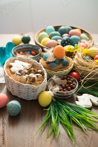 Colorful Easter eggs in nest, feathers and spring flowers on wooden table. Easter holiday decorations , Easter concept background.