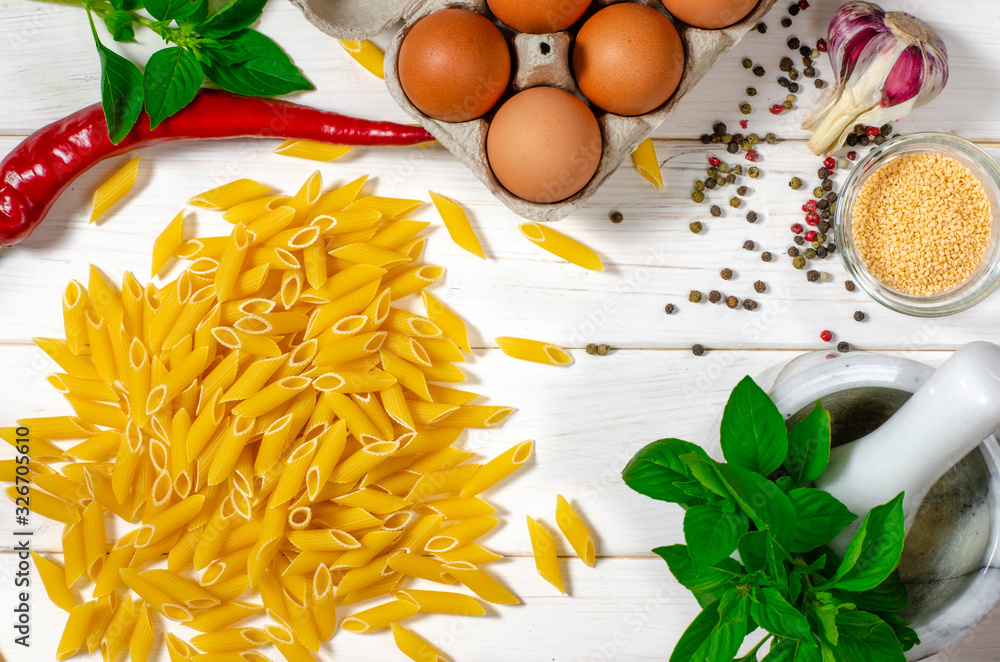 Ingredients for the preparation of penne pasta lie on a white wooden table