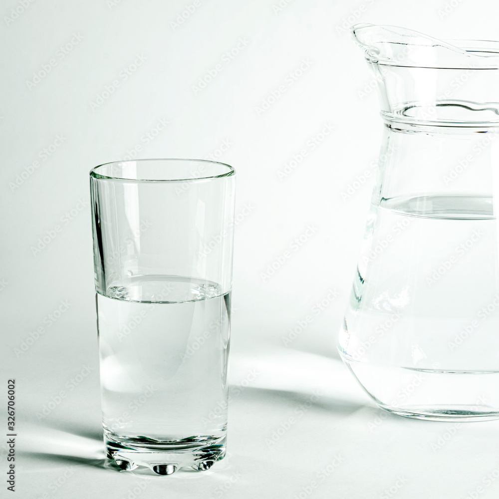 Pure clear water in a glass and jug stands on a white background Pure clear water in a glass and jug stands on a white background