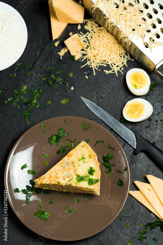 pancake with cheese, herbs and egg for Shrovetide. the pancake is cut into pieces and sprinkled with cheese . on dark background