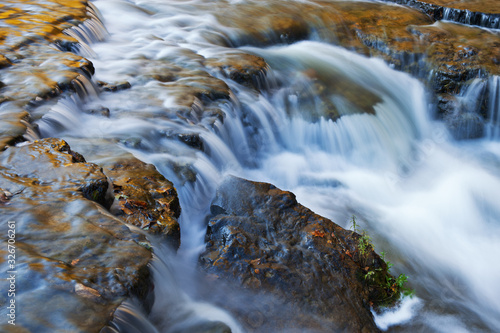 Landscape of a cascade at Autrain Falls captured with motion blur and illuminated by reflected color from sunlit autumn maples, Michigan's Upper Peninsula, USA photo