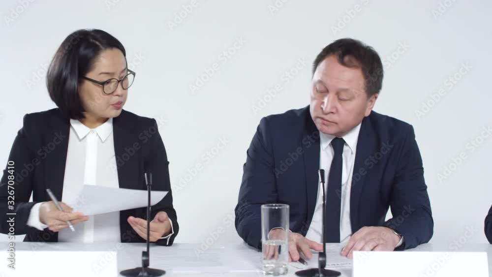 Tracking right of two brunette women and middle-aged Asian man wearing elegant clothes sitting at table during conference meeting and signing contract Tracking right of two brunette women and middle-aged Asian man wearing elegant clothes sitting at table during conference meeting and signing contract