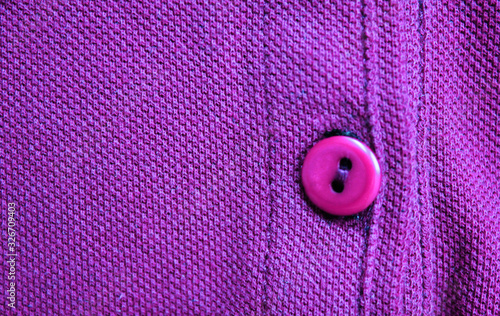 Button on violet cloth texture background. Simple button close up, colorful purple cotton cloth material, casual clothing fragment, jacket fabric top view 