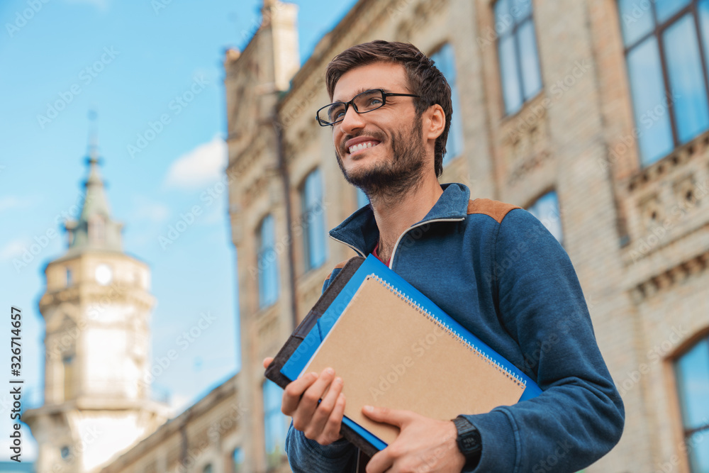 © InsideCreativeHouse - Young caucasian male student with books outside near campus