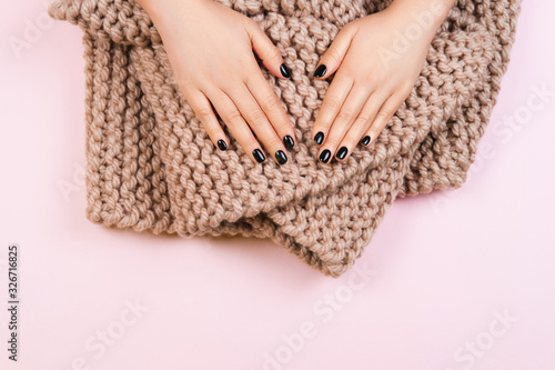 Black manicure with cozy wool knitted scarf on pastel background. Hygge style