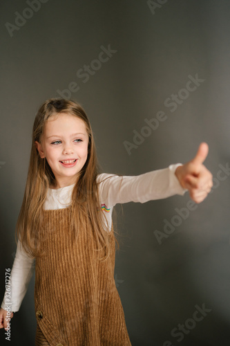 Funny little girl showing her finger like thumbs up, positive portrait of little girl on gray background, girl expreses cool photo