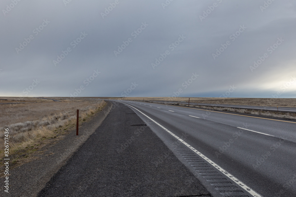 Curving empty highway cutting through vast open field on overcast day