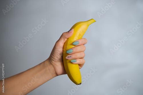 Female hand with creative manicure in pastel colors holds a yellow banana on a pink background.