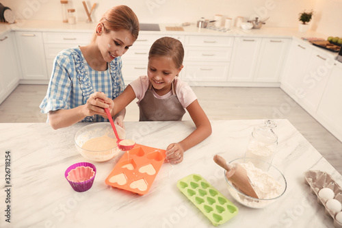 Mother and daughter making cupcakes together in kitchen