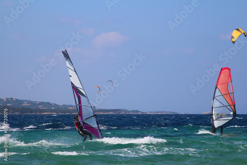 Windsurfers and kitesurfers planing over the emerald green water of Sardinia (Porto Pollo, Italy)