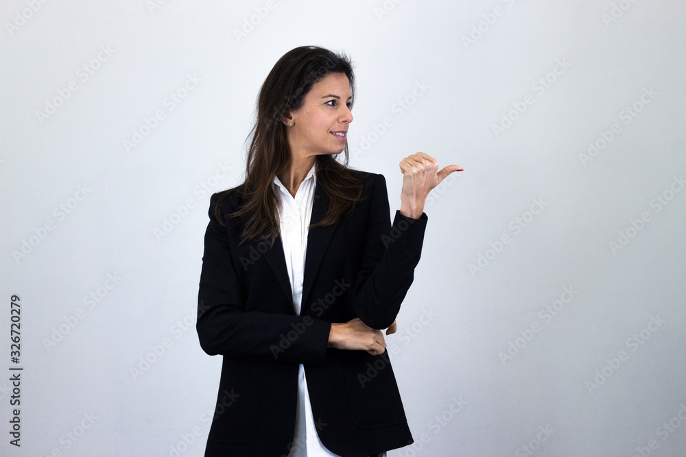 happy positive caucasian bussiness woman smiling pointing aside with index finger and looking aside, having great idea, isolated on gray background studio shot, white shirt and black jacket, dark air. happy positive caucasian bussiness woman smiling pointing aside with index finger and looking aside, having great idea, isolated on gray background studio shot, white shirt and black jacket, dark air.