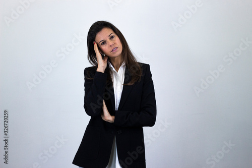 Portrait of worried attractive bussiness woman model keeps hand on forhead, isolated on gray background studio shot, white shirt and black jacket, dark air. Place for your text in copy space.