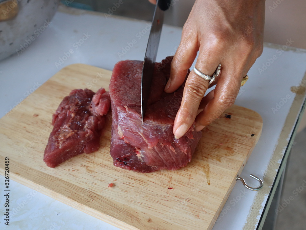female hands slicing raw beef fillet for steak on wooden board.