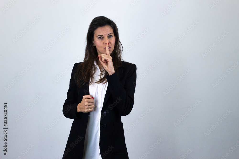 Portrait of attractive caucasian bussiness woman model holding index finger near his lips, isolated on gray background studio shot, white shirt and black jacket, dark air. Place for your text in copy Portrait of attractive caucasian bussiness woman model holding index finger near his lips, isolated on gray background studio shot, white shirt and black jacket, dark air. Place for your text in copy