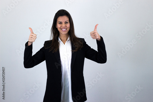 Portrait of happy confidence caucasian bussiness woman showing thumbs up gesture, isolated on gray background studio shot, white shirt and black jacket, dark air. Place for your text in copy space.