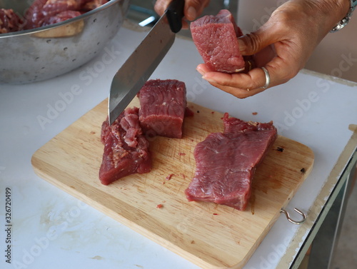 female hands slicing raw beef fillet for steak on wooden board.