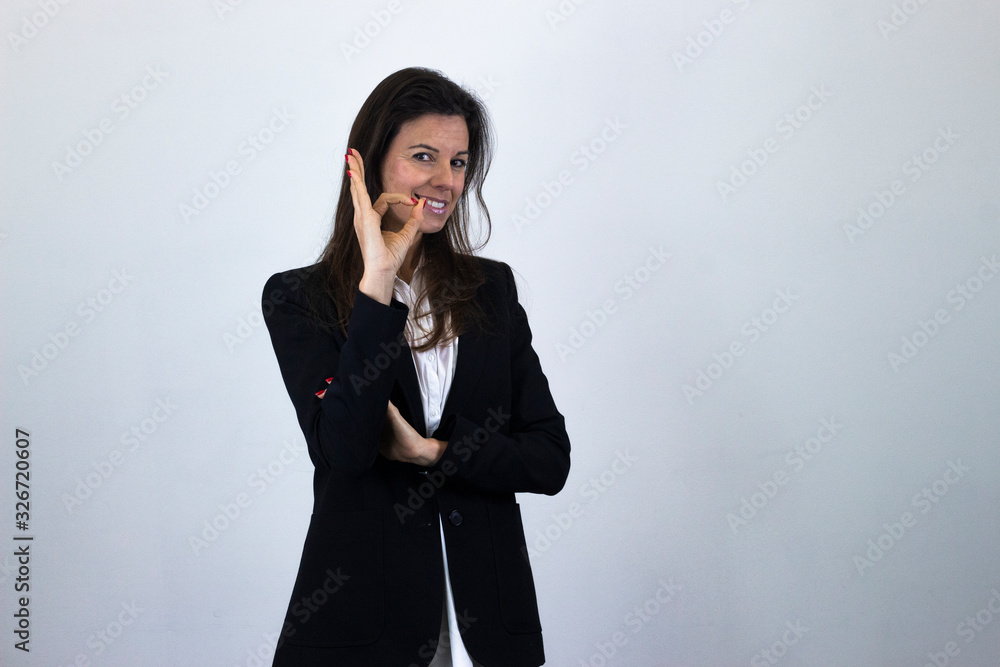 Portrait of positive caucasian bussiness woman showing ok sign with hand and fingers, has satisfied facial expression, isolated on gray background studio shot, white shirt and black jacket, dark air. Portrait of positive caucasian bussiness woman showing ok sign with hand and fingers, has satisfied facial expression, isolated on gray background studio shot, white shirt and black jacket, dark air.