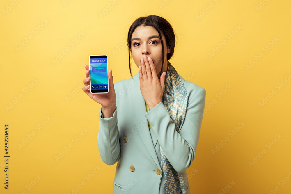 surprised african american girl covering face and holding smartphone with booking app on yellow surprised african american girl covering face and holding smartphone with booking app on yellow
